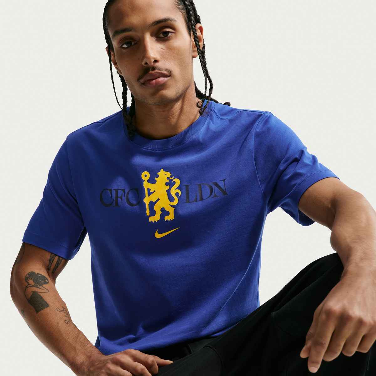 Man wearing a blue t-shirt with a logo and text, sitting against a plain background