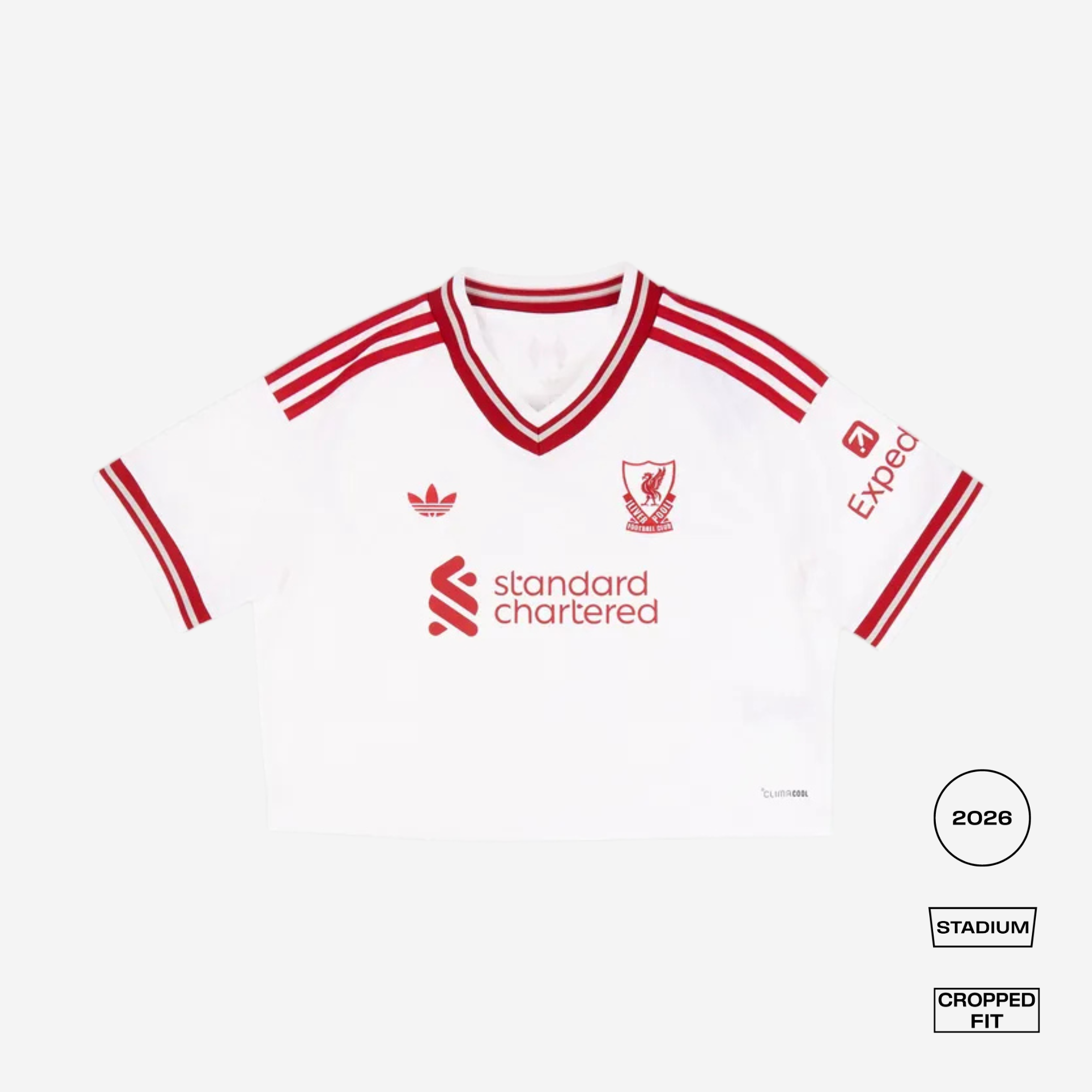 A white cropped short-sleeve football jersey with red stripes and logos, featuring the Liverpool FC crest, Adidas logo, Standard Chartered sponsor, and Expedia sleeve print, shown on a light gray background with fit labels in the lower right.