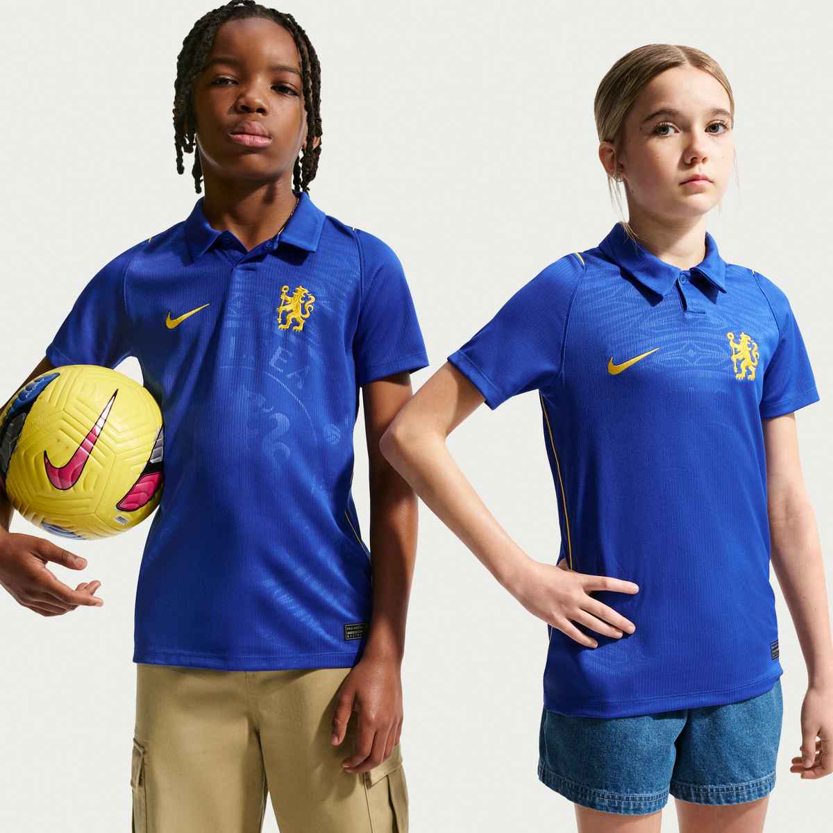 Two children wearing blue sports jerseys with a lion emblem and Nike logo, holding a yellow soccer ball.